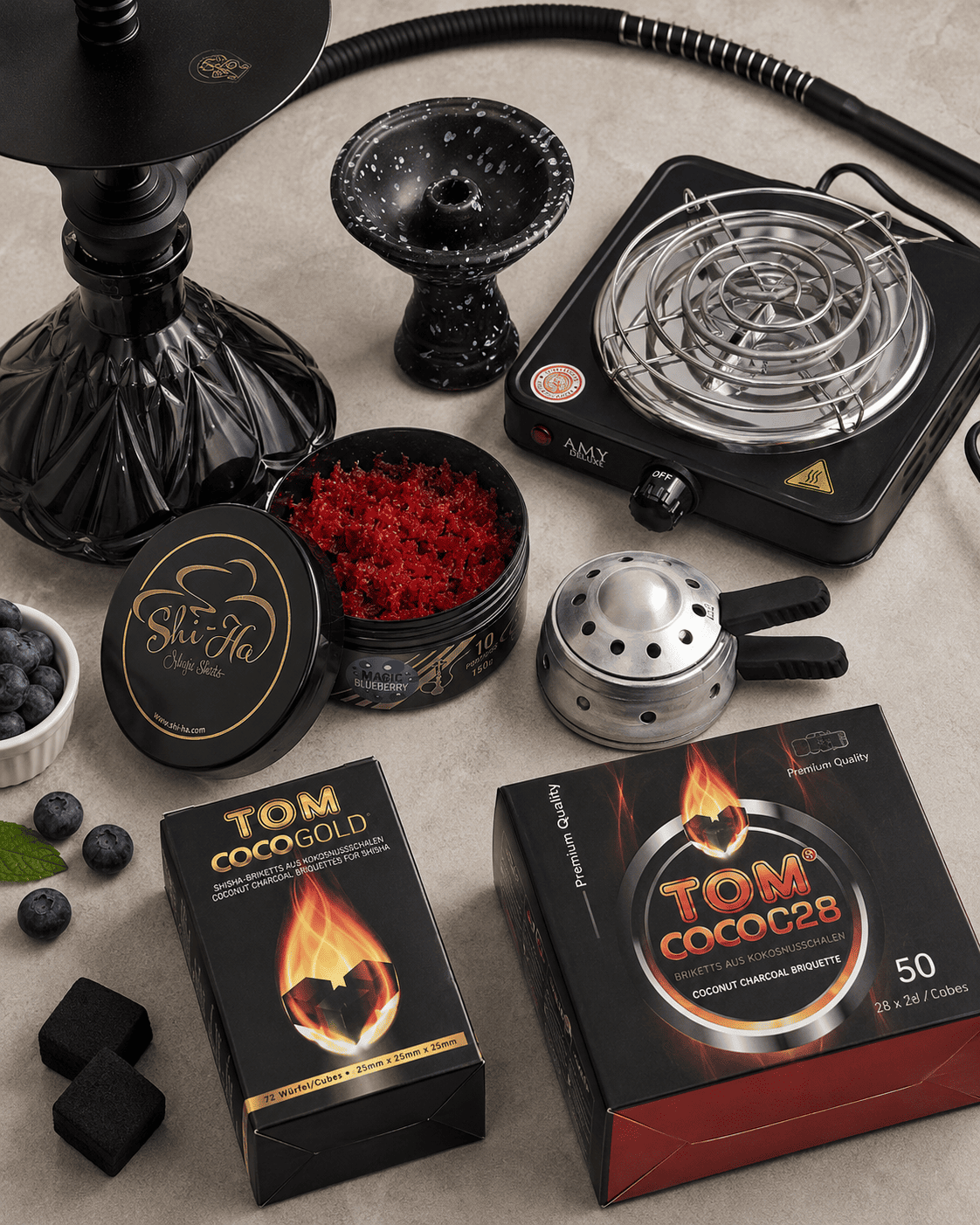 Pot met rode shisha smaak naast natuurlijke kokoskolen, een waterpijp tabakskop, kolenbrander en TOM Coco kolen. Zo kies je de juiste smaak en kolen voor je sessie.